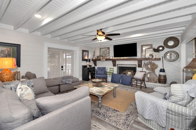 living room featuring a brick fireplace, hardwood / wood-style flooring, ceiling fan, and beam ceiling