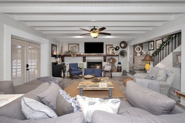 living room featuring ceiling fan, beamed ceiling, and a brick fireplace