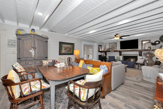 dining area featuring a large fireplace, light hardwood / wood-style floors, beamed ceiling, and ceiling fan