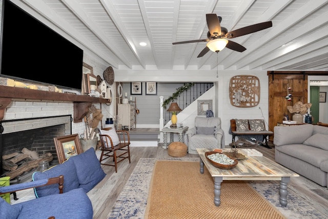 living room featuring a brick fireplace, wood walls, ceiling fan, beam ceiling, and light wood-type flooring