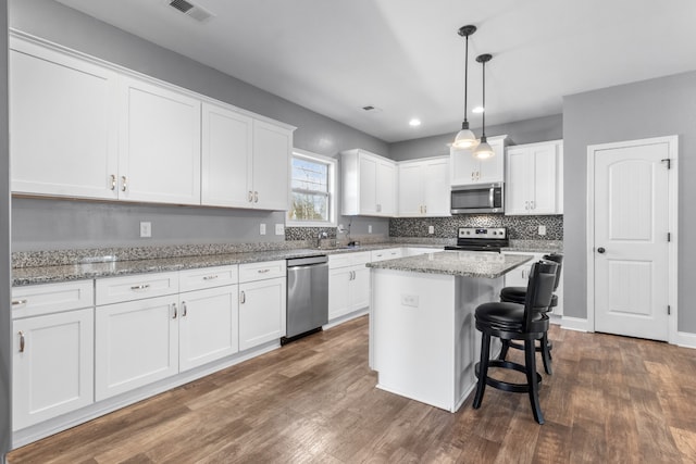 kitchen with decorative light fixtures, a kitchen island, white cabinetry, and stainless steel appliances