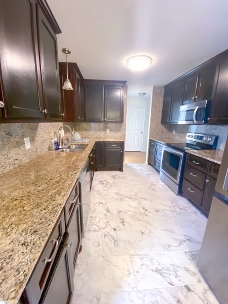 kitchen featuring light stone counters, sink, pendant lighting, and appliances with stainless steel finishes