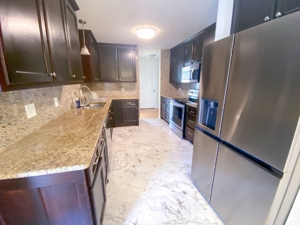 kitchen featuring sink, appliances with stainless steel finishes, light stone countertops, hanging light fixtures, and decorative backsplash