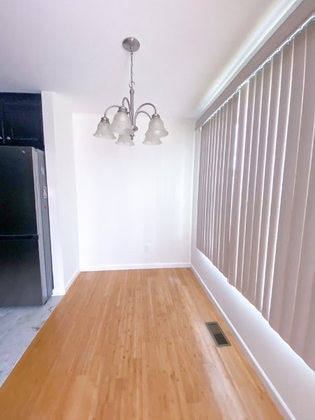 unfurnished dining area featuring wood-type flooring and an inviting chandelier