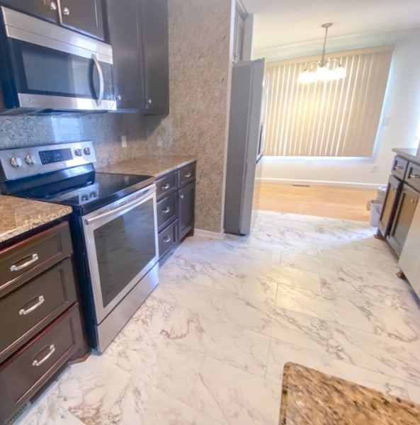 kitchen featuring dark brown cabinetry, appliances with stainless steel finishes, light stone countertops, hanging light fixtures, and a chandelier