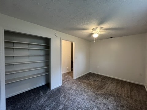 unfurnished bedroom with ceiling fan, a textured ceiling, and dark carpet