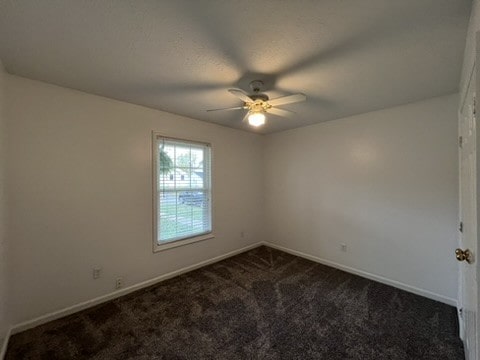 spare room with dark colored carpet and ceiling fan