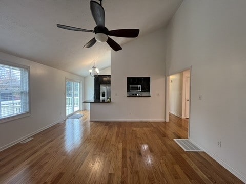 unfurnished living room featuring ceiling fan with notable chandelier, lofted ceiling, and dark hardwood / wood-style floors