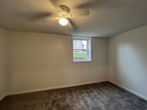 empty room featuring ceiling fan, a textured ceiling, and dark carpet