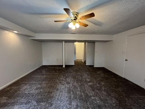 interior space with a textured ceiling, dark colored carpet, and ceiling fan