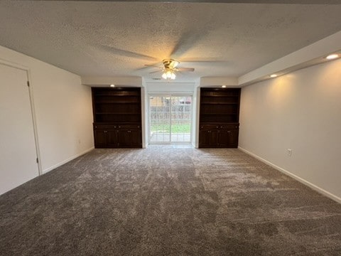 empty room with a textured ceiling, dark colored carpet, and ceiling fan