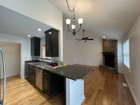 kitchen with ceiling fan with notable chandelier, light hardwood / wood-style floors, sink, stainless steel dishwasher, and a fireplace