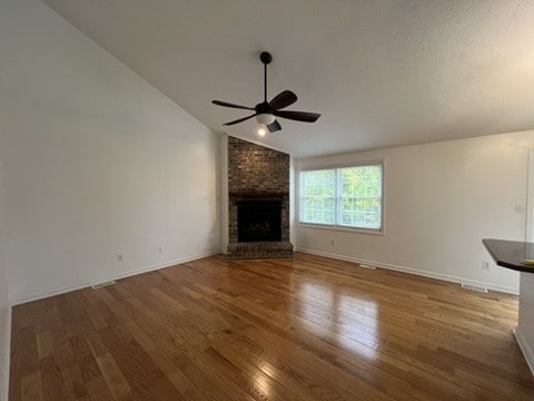 unfurnished living room with hardwood / wood-style floors, a fireplace, ceiling fan, and vaulted ceiling