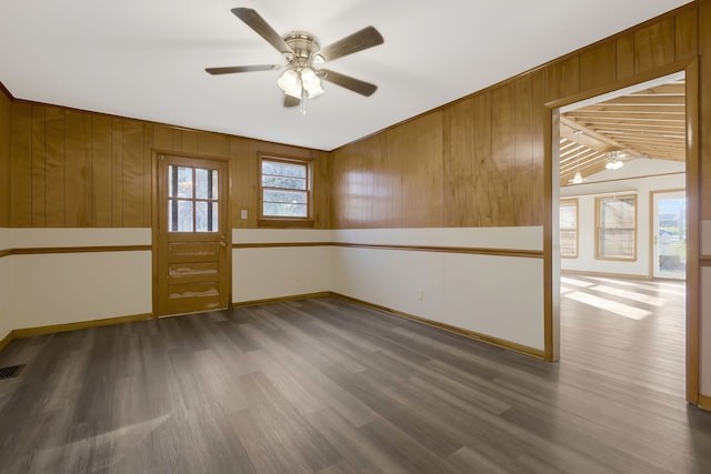 unfurnished room with dark hardwood / wood-style floors, ceiling fan, wooden walls, and vaulted ceiling