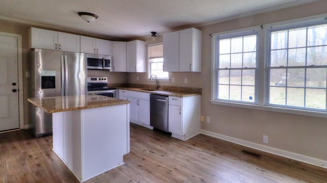 kitchen with appliances with stainless steel finishes, white cabinets, light hardwood / wood-style floors, a center island, and sink