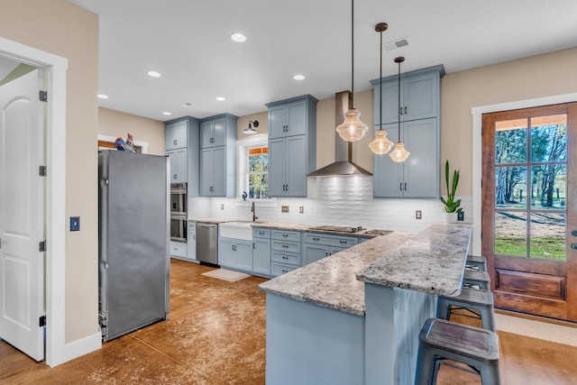 kitchen featuring a breakfast bar, hanging light fixtures, appliances with stainless steel finishes, tasteful backsplash, and wall chimney range hood