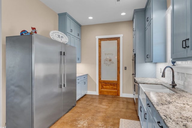 kitchen with light stone countertops, appliances with stainless steel finishes, tasteful backsplash, blue cabinets, and sink