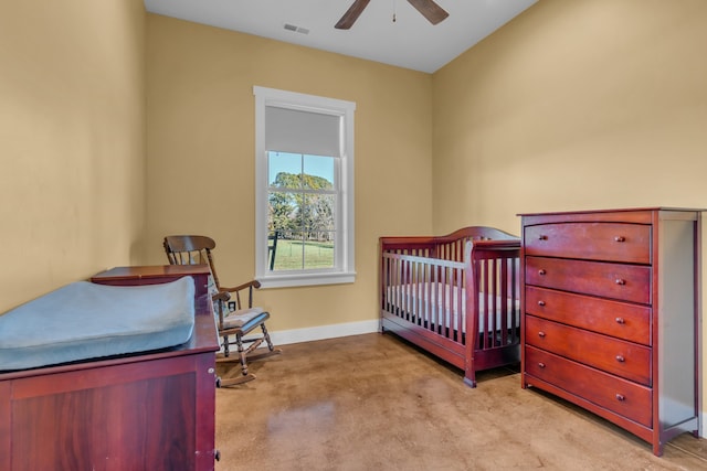 bedroom featuring ceiling fan, a nursery area, and light carpet