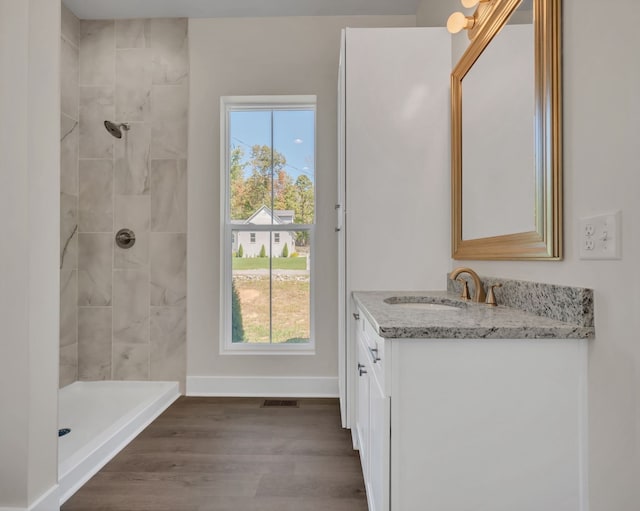 bathroom featuring hardwood / wood-style floors, vanity, a healthy amount of sunlight, and a tile shower