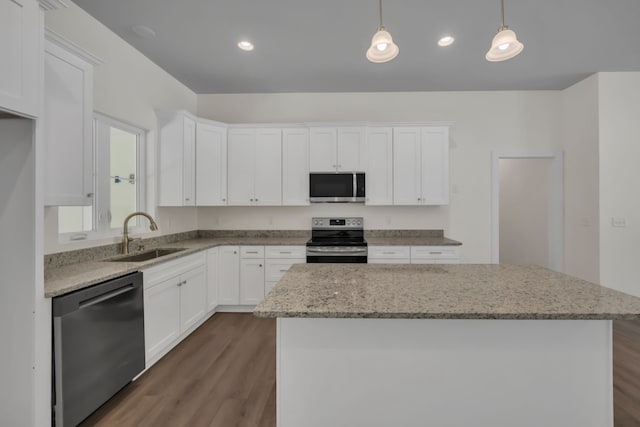 kitchen with stainless steel appliances, sink, a kitchen island, pendant lighting, and white cabinetry