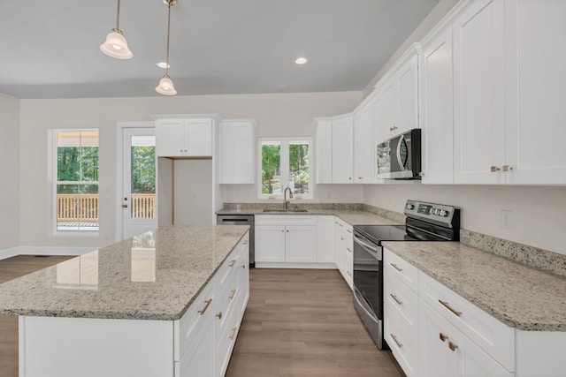 kitchen featuring stainless steel appliances, a healthy amount of sunlight, a center island, white cabinetry, and decorative light fixtures