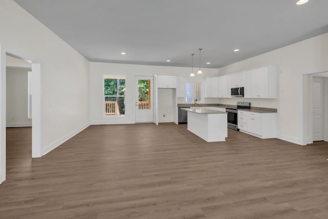 kitchen featuring stainless steel appliances, white cabinetry, hanging light fixtures, hardwood / wood-style floors, and a center island