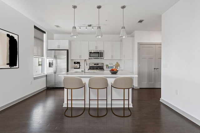 kitchen with a kitchen island with sink, stainless steel appliances, white cabinets, and pendant lighting