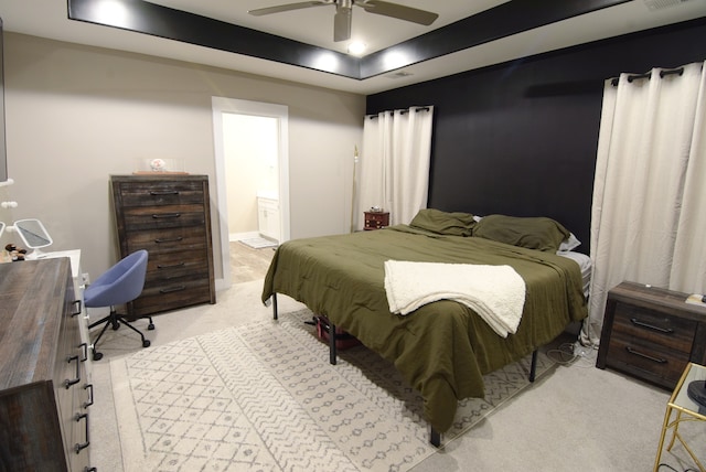 bedroom with a raised ceiling, ceiling fan, light colored carpet, and connected bathroom