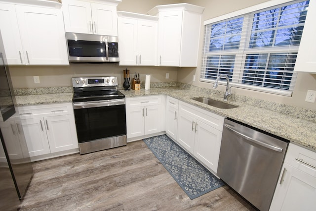 kitchen featuring white cabinets, sink, light stone countertops, light wood-type flooring, and appliances with stainless steel finishes