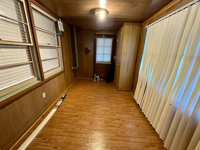 corridor with wood walls, a healthy amount of sunlight, and light wood-type flooring