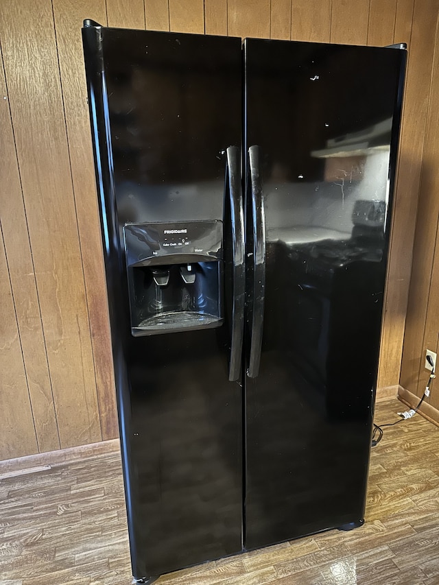 room details featuring black fridge with ice dispenser, wood-type flooring, and wooden walls