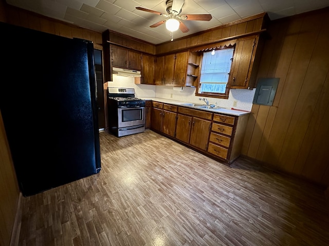 kitchen with light hardwood / wood-style floors, sink, tasteful backsplash, stainless steel gas range oven, and wooden walls