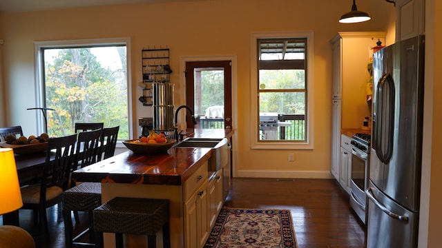 kitchen featuring decorative light fixtures, dark wood-type flooring, stainless steel appliances, sink, and a breakfast bar