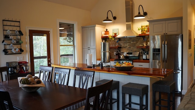 kitchen with a kitchen breakfast bar, vaulted ceiling, exhaust hood, butcher block counters, and stainless steel appliances