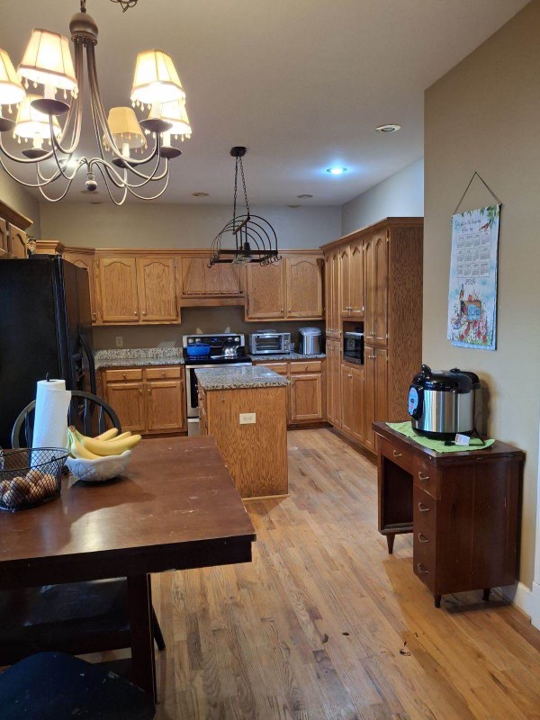 kitchen with stainless steel electric range, a center island, black refrigerator, pendant lighting, and light hardwood / wood-style flooring