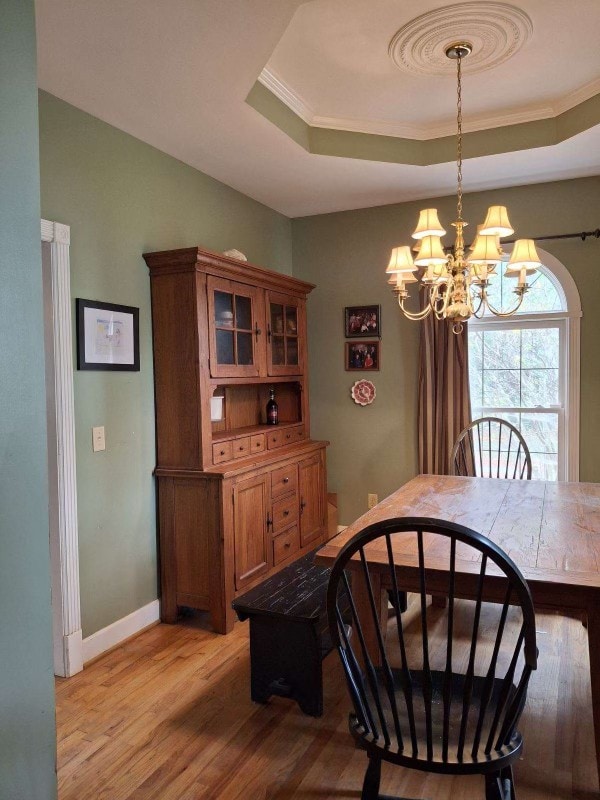 dining area with a chandelier, ornamental molding, light wood-type flooring, and a tray ceiling