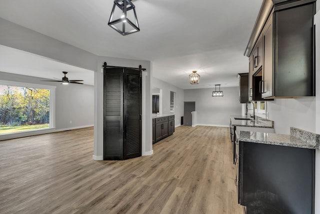 kitchen with light stone countertops, a barn door, light hardwood / wood-style flooring, decorative light fixtures, and dark brown cabinets