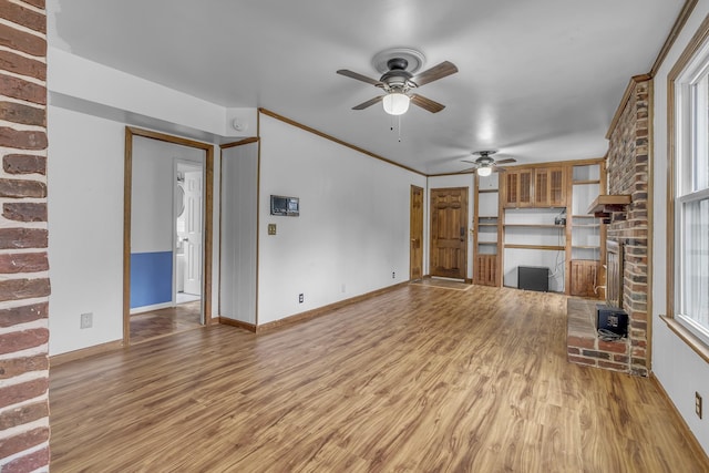 unfurnished living room featuring crown molding, a wood stove, ceiling fan, and light wood-type flooring