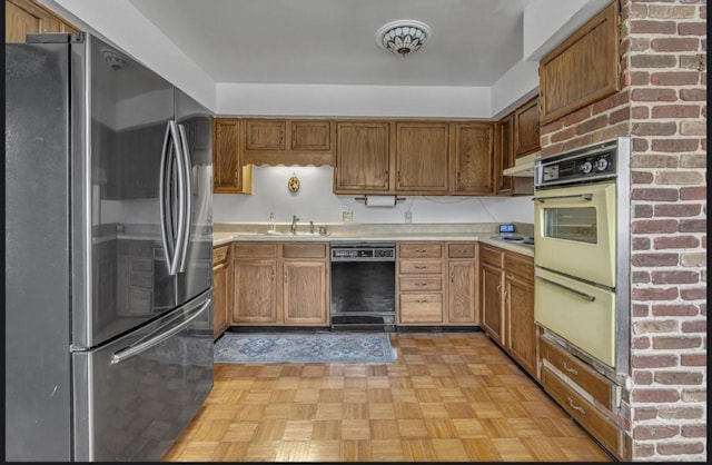 kitchen with sink, light parquet flooring, stainless steel refrigerator, and black dishwasher