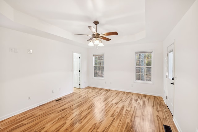 empty room with ceiling fan, a tray ceiling, and light hardwood / wood-style flooring