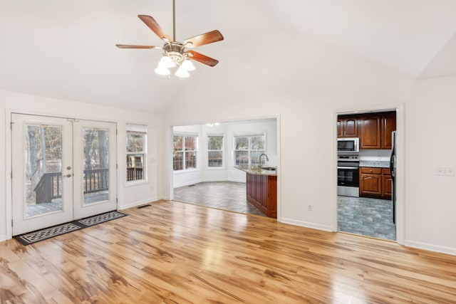 unfurnished living room featuring high vaulted ceiling, french doors, sink, ceiling fan, and light wood-type flooring