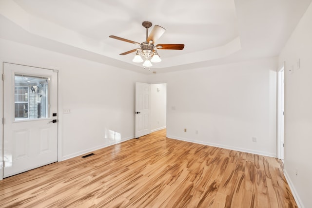 empty room featuring ceiling fan, light hardwood / wood-style floors, and a raised ceiling