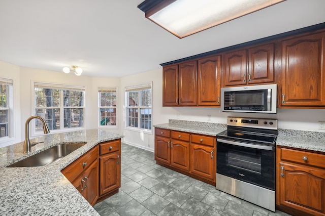 kitchen with plenty of natural light, light stone counters, sink, and appliances with stainless steel finishes