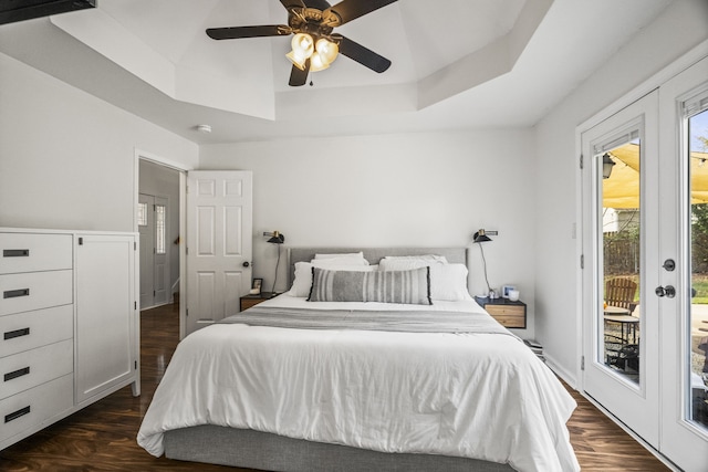 bedroom featuring dark hardwood / wood-style flooring, access to outside, a tray ceiling, and ceiling fan