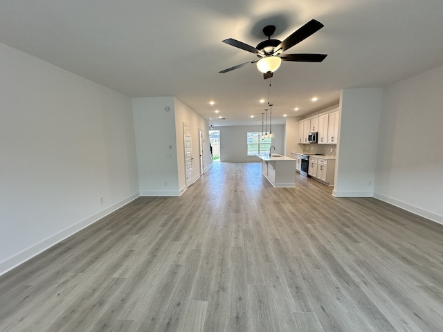 unfurnished living room featuring light hardwood / wood-style floors, ceiling fan, and sink