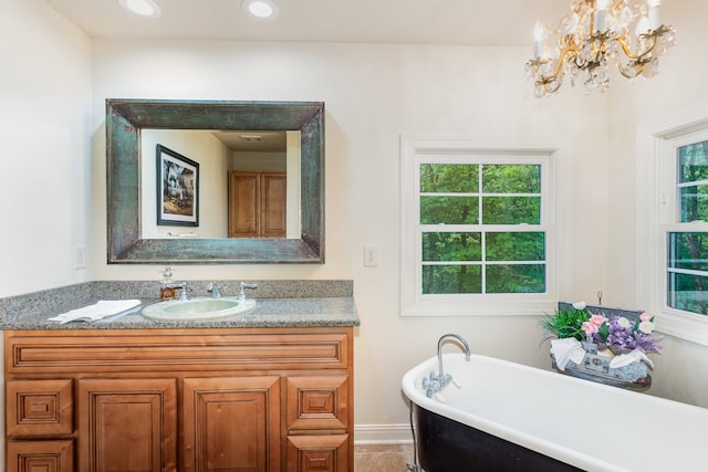 bathroom with a bath, a healthy amount of sunlight, an inviting chandelier, and vanity