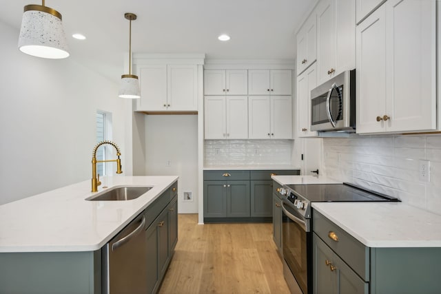 kitchen with white cabinetry, appliances with stainless steel finishes, hanging light fixtures, sink, and light hardwood / wood-style floors