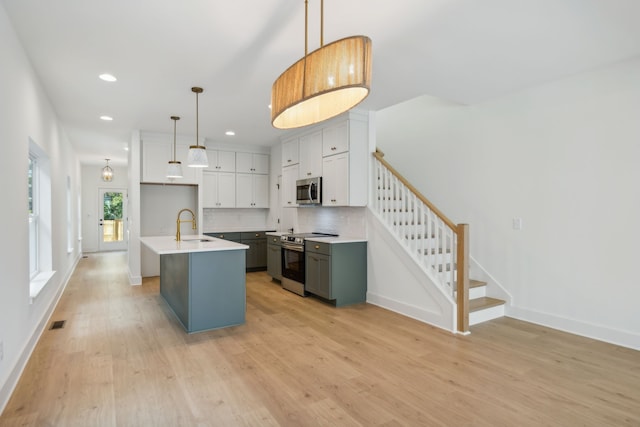 kitchen featuring an island with sink, decorative light fixtures, appliances with stainless steel finishes, and light hardwood / wood-style flooring