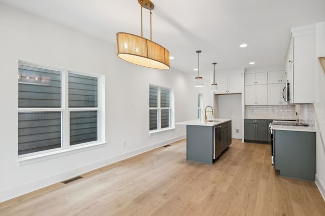 kitchen with a center island with sink, appliances with stainless steel finishes, hanging light fixtures, gray cabinets, and light wood-type flooring