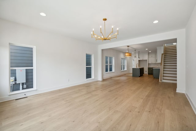 unfurnished living room featuring light wood-type flooring and an inviting chandelier